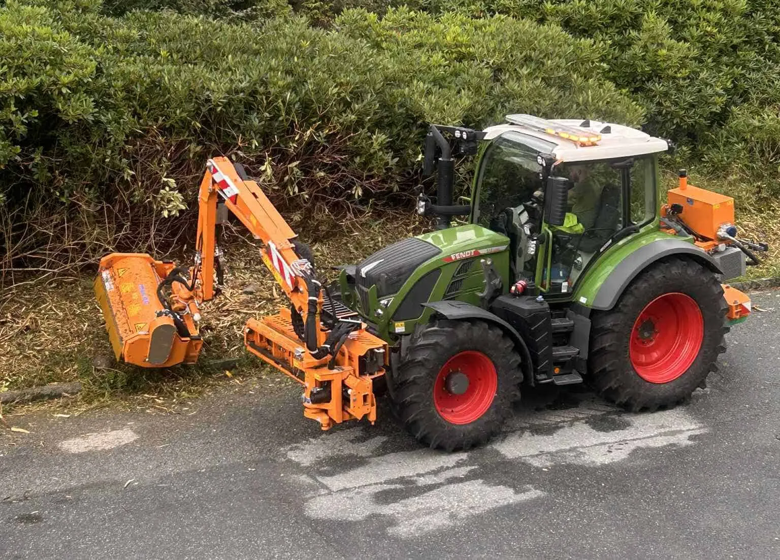 Traktor med klippearm som beskjærer en hekk langs veien